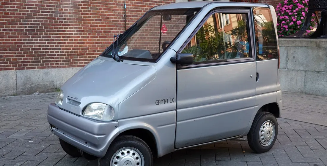 Voiturette électrique quatre places compacte stationnée en ville, portes ouvertes, ambiance urbaine lumineuse